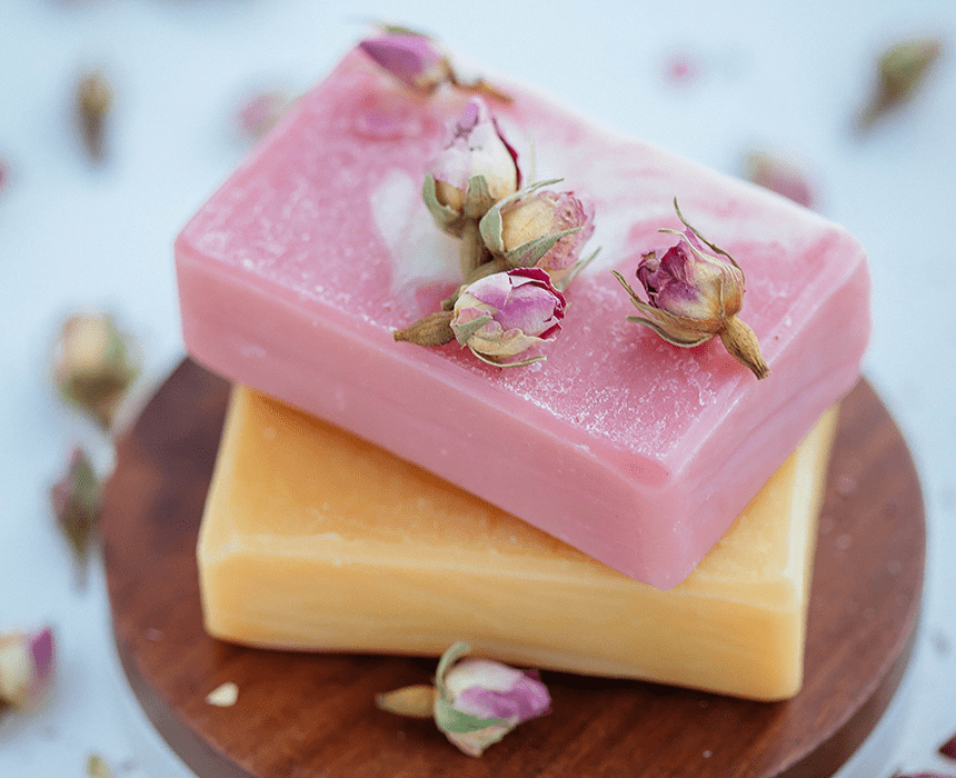 Two soaps with flowers on them sitting on a wooden board.